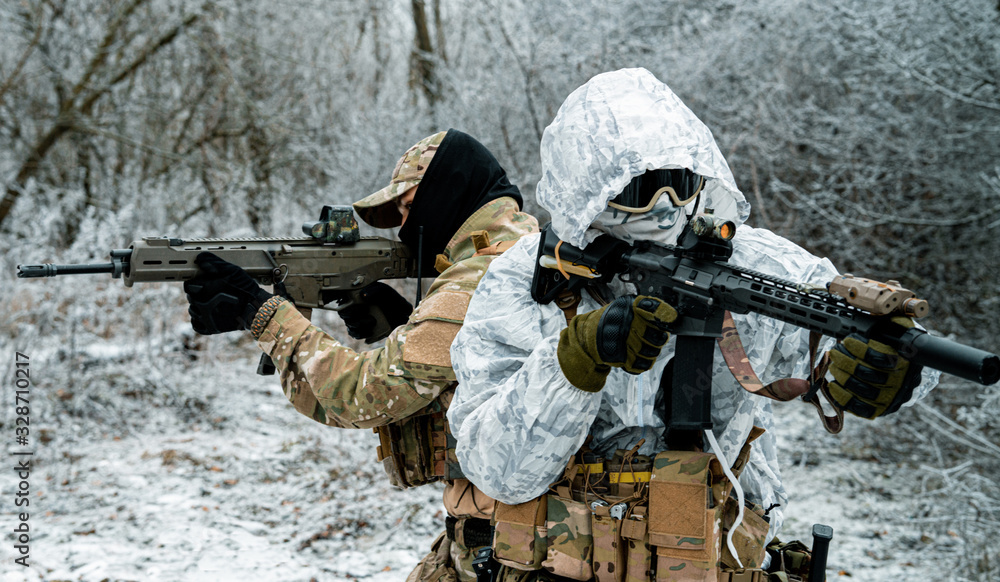 Fototapeta premium Two men in camouflage white, green uniform with machineguns back to back. Soldiers with muchinegun in the winter forest. Horizontal photo, side view.