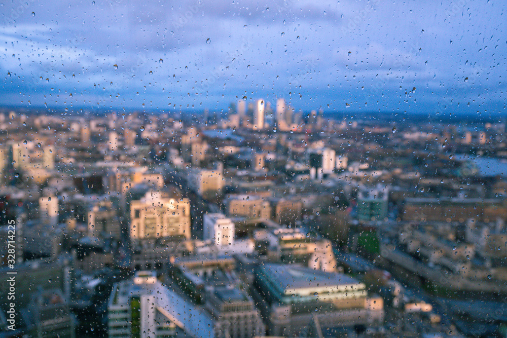 Obraz premium Raindrops on a window pane of glass with blurred background of River Thames and City of London Canary Wharf financial district