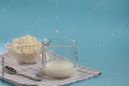 Fresh cottage cheese in a transparent bowl with a spoon and a glass in which a stream of kefir is poured on a blue background. Fermented foods. Good bacteria for health.