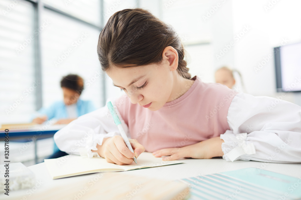 Caucasian female middle schooler with dark brown hair sitting at school desk writing essay, horizontal medium close up portrait Caucasian female middle schooler with dark brown hair sitting at school desk writing essay, horizontal medium close up portrait