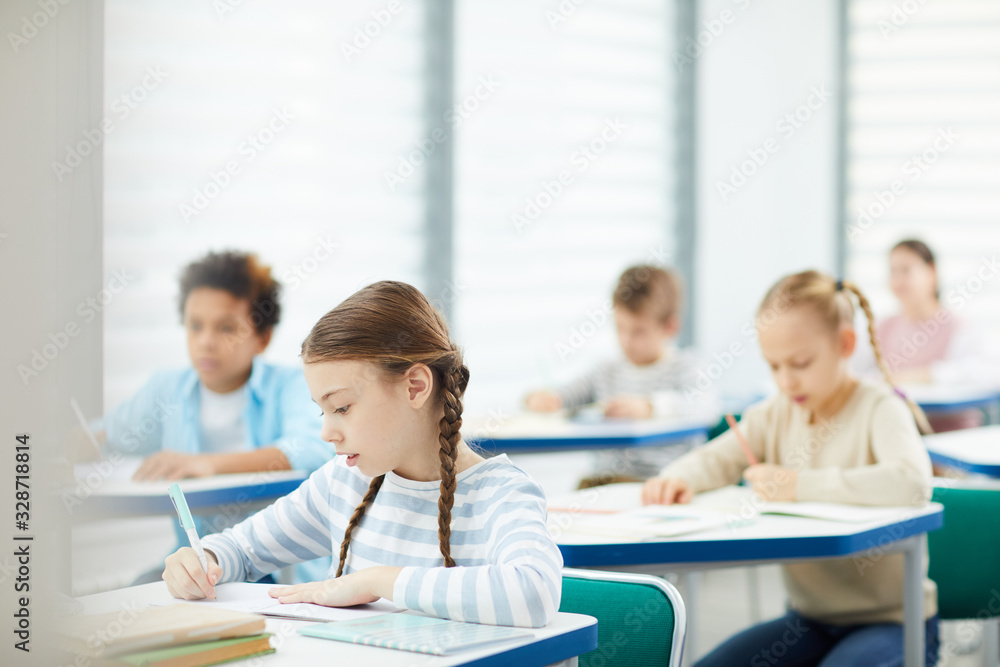 Horizontal Caucasian girl focused shot of primary school students doing lesson tasks in modern classroom, copy space