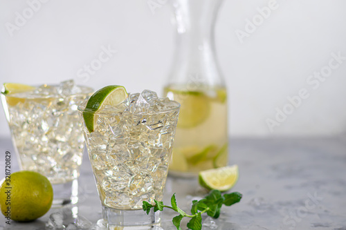 Glasses are filled with ice and cold green tea. Garnished with lime slices and a sprig of mint. On a light background.