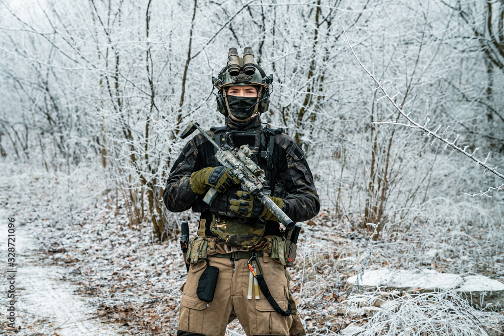 Fototapeta premium Airsoft man in black camouflage uniform and short machinegun with optical sight. Soldier in the winter forest. Horizontal photo front view.