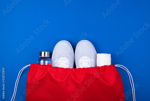 White sport shoes sneakers, glass water bottle and towel in red sport bag on cyan blue background.