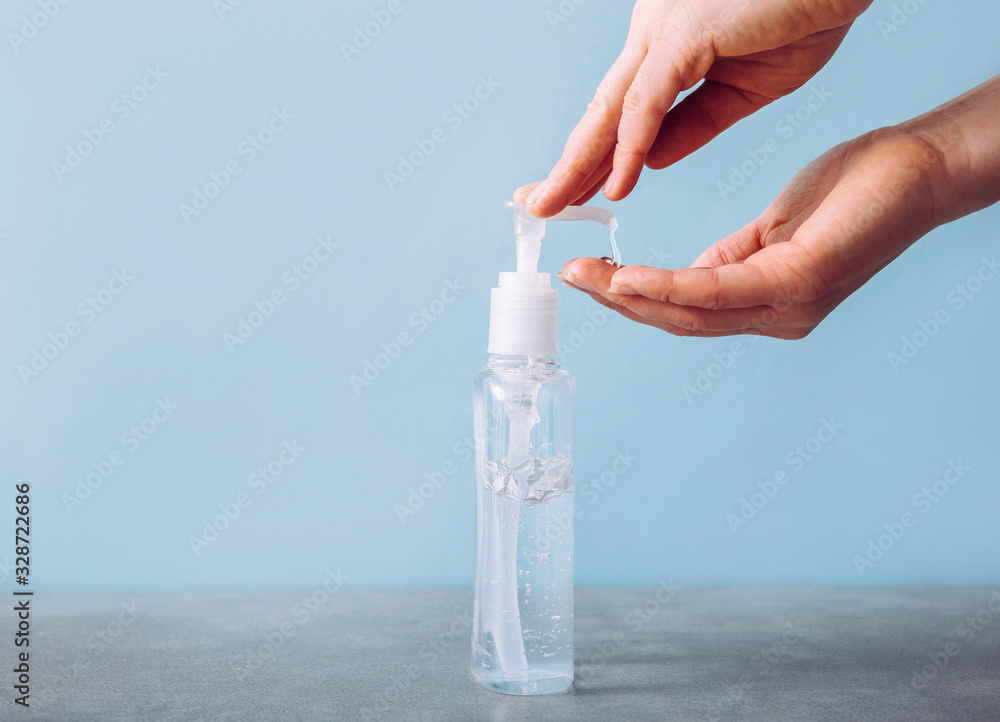 Close up view of woman using hand sanitizer dispenser, blue clean minimalist background. Health concerns concept. - obrazy, fototapety, plakaty 