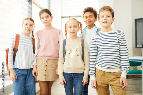 Portrait of stylish boys and girls standing together in school corridor looking at camera, horizontal medium long shot
