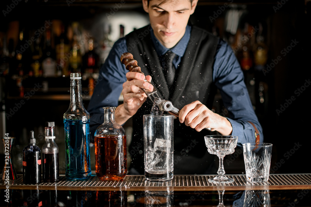 Young bartender splits pieces of ice to make a cocktail.