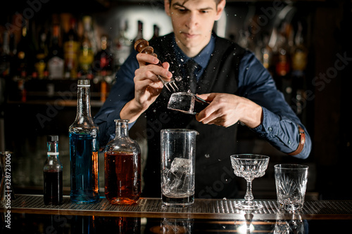 Young bartender professionally splits pieces of ice to make a cocktail.