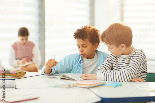 Horizontal portrait of two middle school male students sitting at desk in modrn classroom completing task together, copy space photo