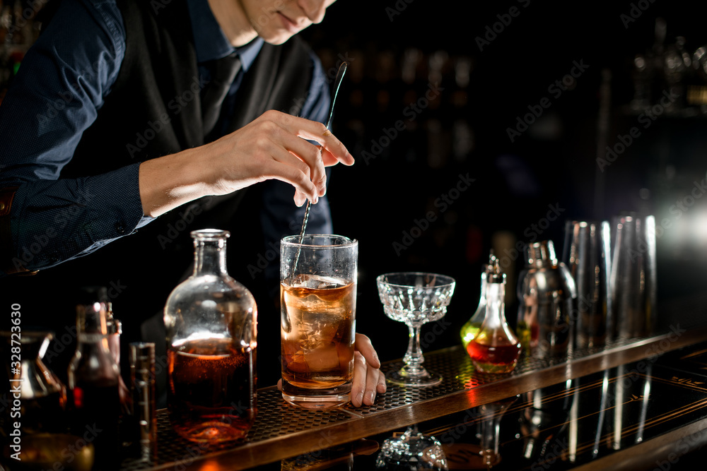 Barman gently stirs cold cocktail with spoon