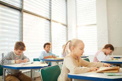 Horizontal shot of young middle school students sitting at desks in modern classroom having lesson, copy space