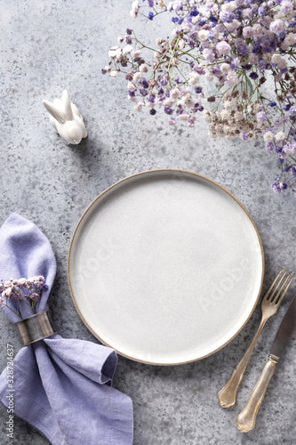 Easter table setting with grey plate and violet decor on grey stone table. Top view. Vertical format.