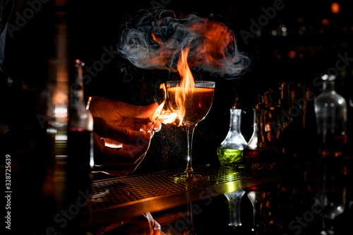 close-up bartender's hands which sets fire near cocktail wineglass.