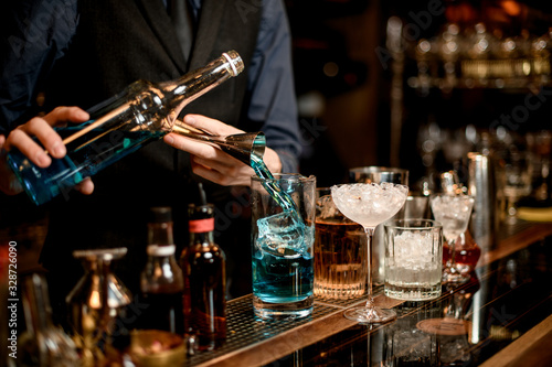 Professional barman makes cold alcoholic cocktail of blue color.