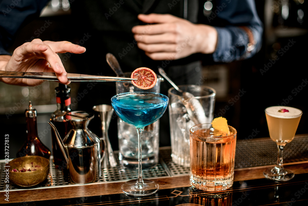 bartender decorates blue cocktail in wineglass with slice of citrus.