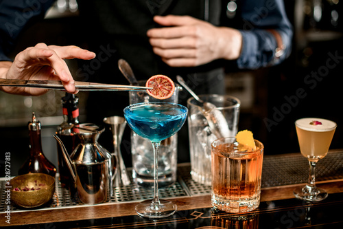bartender decorates blue cocktail in wineglass with slice of citrus.