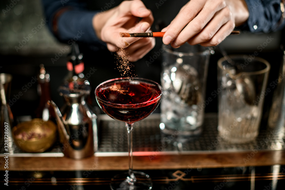 Barman add seasoning to red cocktail in wineglass