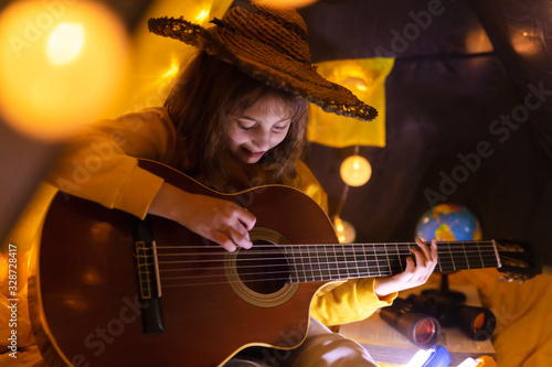 Little girl playing acoustic guitar under the tent in a living room.