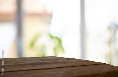 An empty wooden tabletop on a window pane and abstract green blur from the garden with a view of the yard, can be used to display or assemble your products (or products).