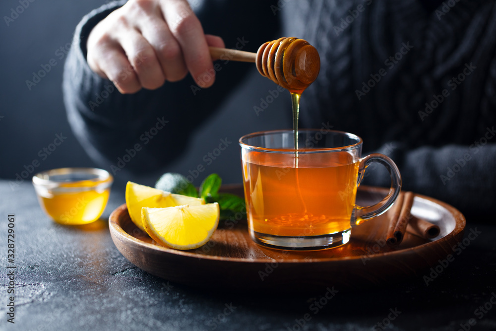 Cup of tea with pouring honey and lemon. Grey background.