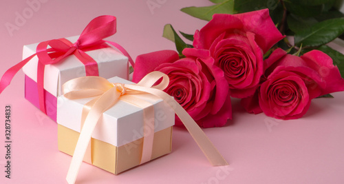 gift boxes multicolored with satin ribbons and three pink floyd roses on a pink background