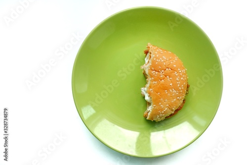 Top eye view of Bite a half of delicious yummy layer burger chicken pepper, pork, egg, cheese, mayonnaise, bun, lettuce in the green plate on a white table background at the kitchen counter.