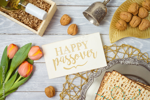 Jewish holiday Passover greeting card with matzo, seder plate, wine and tulip flowers on wooden table.