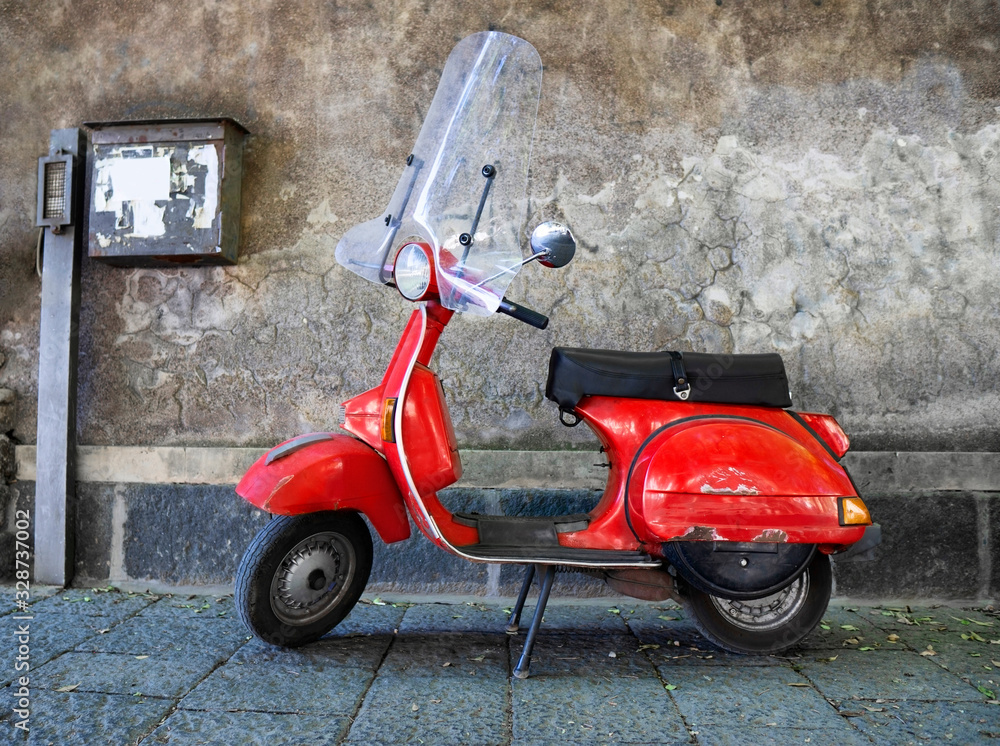 Vintage red scooter parked on a sidewalk by a concrete wall in the city of Catania, Italy.