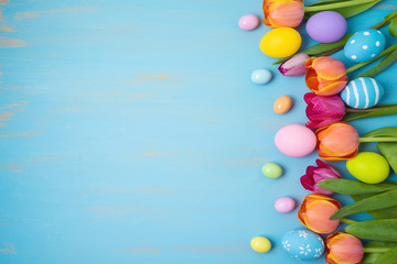 Easter holiday background with easter eggs and tulip flowers on wooden table. Top view from above