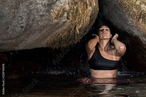 Joven morena de pelo bajo la cascada en una cueva en las montañas al aire libre.