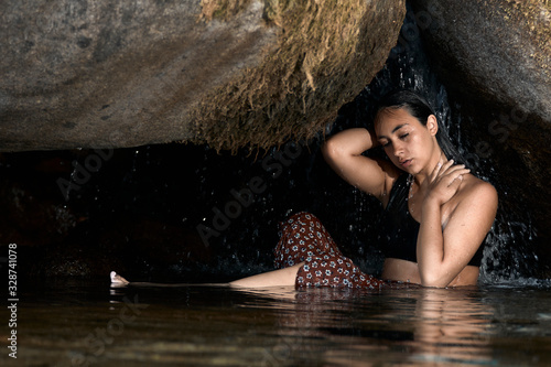 Joven morena de pelo bajo la cascada en una cueva en las montañas al aire libre.