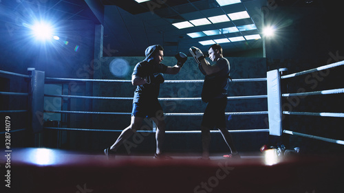 Фотография Professional boxers with gloves train fights in indoor boxing ring, dark colors