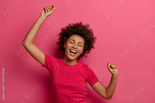 Tableau sur toile Optimistic carefree curly young woman raises arms and dances to favorite awesome