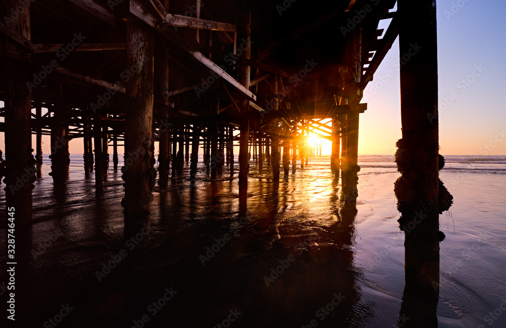 Setting sun shines through the pilings under Crystal Pier at low tide