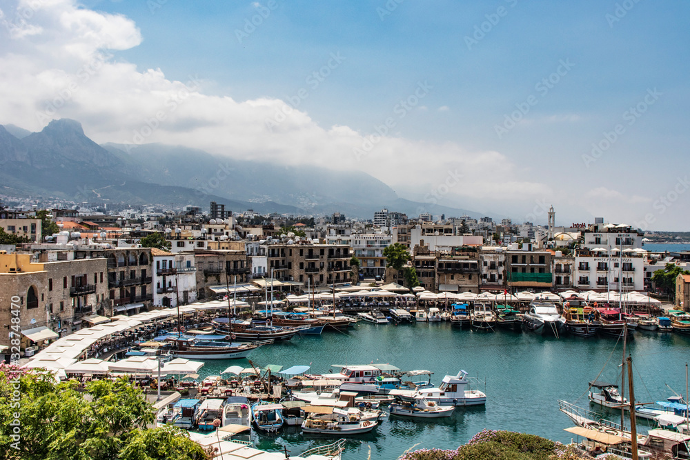 beautiful view of kyrenia harbour, ship, buildings, mountains and blue sky with clouds on the background