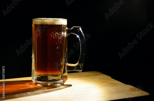 Beer mug with dark beer on a black background, illuminated by a lamp. Bubbles in a liquid. Concept - natural product, pub, splash