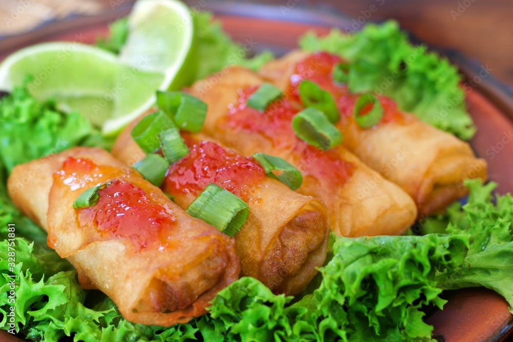 Close up view of spring rolls on a bed of lettuce and drizzled with sweet chilly sauce and sprinkled with spring onions and lime on the side