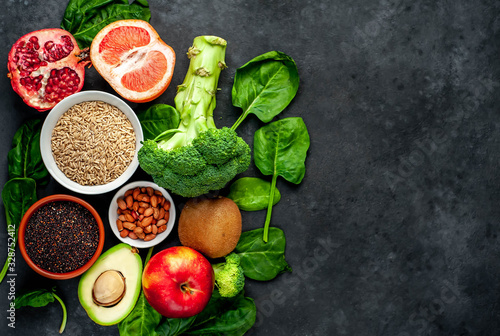Selection of healthy food: fruits, seeds, cereals, superfoods, vegetables, leafy vegetables on a stone background. Healthy food for humans. Copy space for your text.