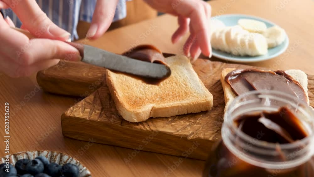 Woman spreading chocolate nut butter on toasted bread. Process of cooking tasty breakfast or lunch sandwich with chocolate nut butter Woman spreading chocolate nut butter on toasted bread. Process of cooking tasty breakfast or lunch sandwich with chocolate nut butter