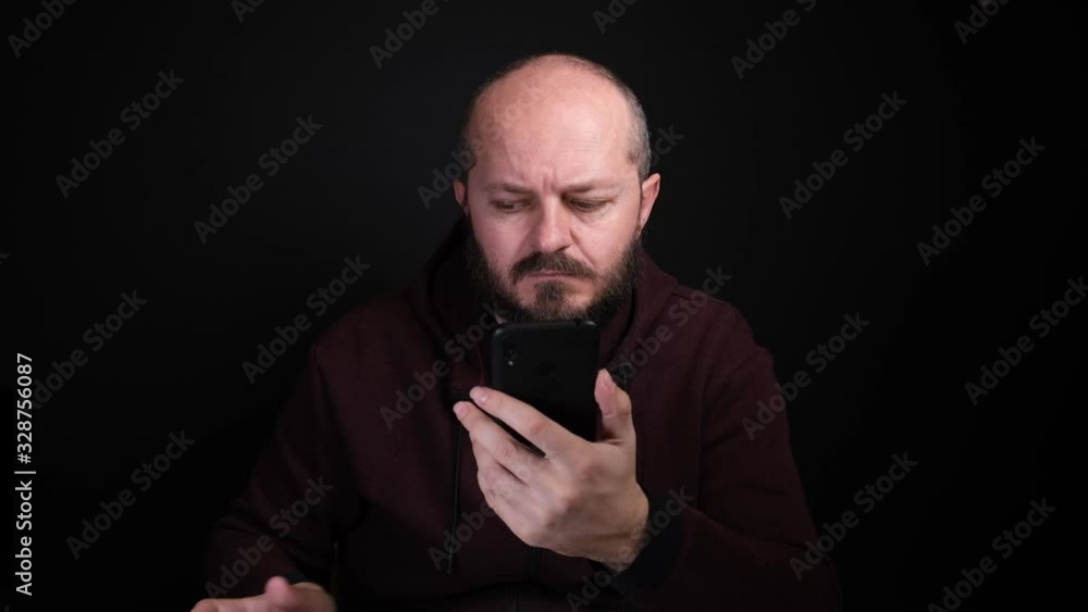 Adult caucasian man in hoodie sitting in front of black background, holding smart phone, typing, drinks coffee
Adult caucasian man in hoodie sitting in front of black background, holding smart phone, typing, drinks coffee