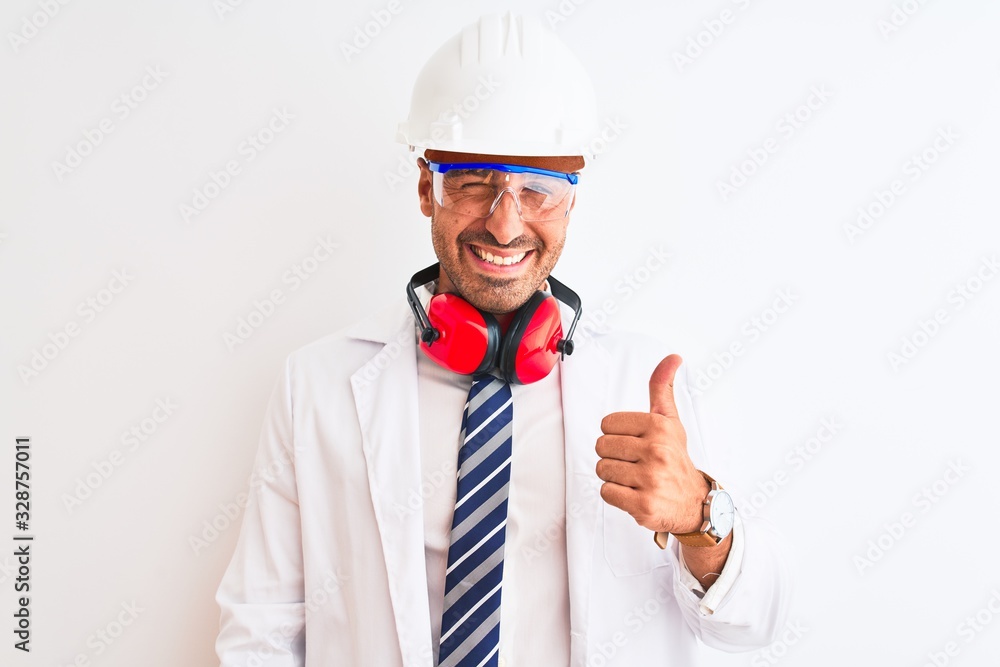 Young chemist man wearing security helmet and headphones over isolated background doing happy thumbs up gesture with hand. Approving expression looking at the camera with showing success. Young chemist man wearing security helmet and headphones over isolated background doing happy thumbs up gesture with hand. Approving expression looking at the camera with showing success.