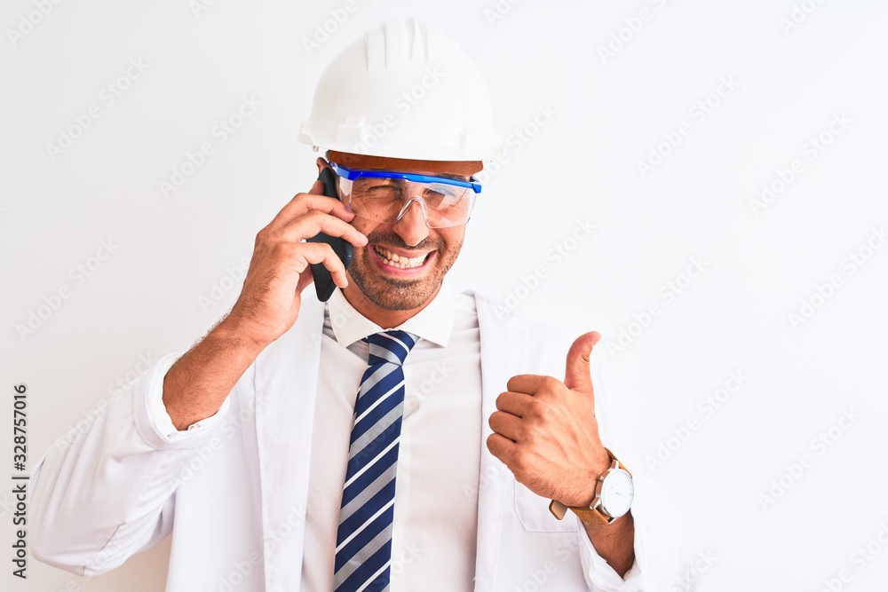 Young scientist man wearing safety helmet and calling using smartphone over isolated background happy with big smile doing ok sign, thumb up with fingers, excellent sign Young scientist man wearing safety helmet and calling using smartphone over isolated background happy with big smile doing ok sign, thumb up with fingers, excellent sign