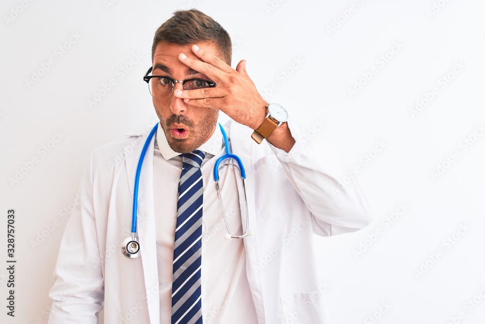 Young handsome doctor man wearing stethoscope over isolated background peeking in shock covering face and eyes with hand, looking through fingers with embarrassed expression. Young handsome doctor man wearing stethoscope over isolated background peeking in shock covering face and eyes with hand, looking through fingers with embarrassed expression.