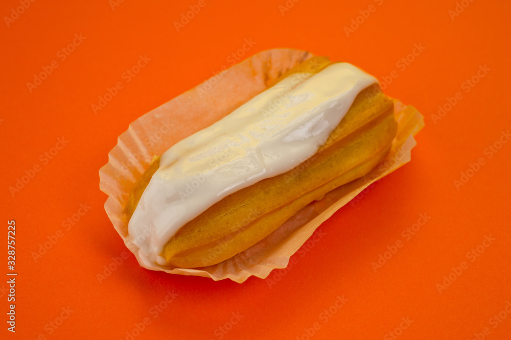 Eclair cake with custard lying on a paper substrate, photographed against a background of orange. Background for cooking and sweets. Eclair cake with custard lying on a paper substrate, photographed against a background of orange. Background for cooking and sweets.
