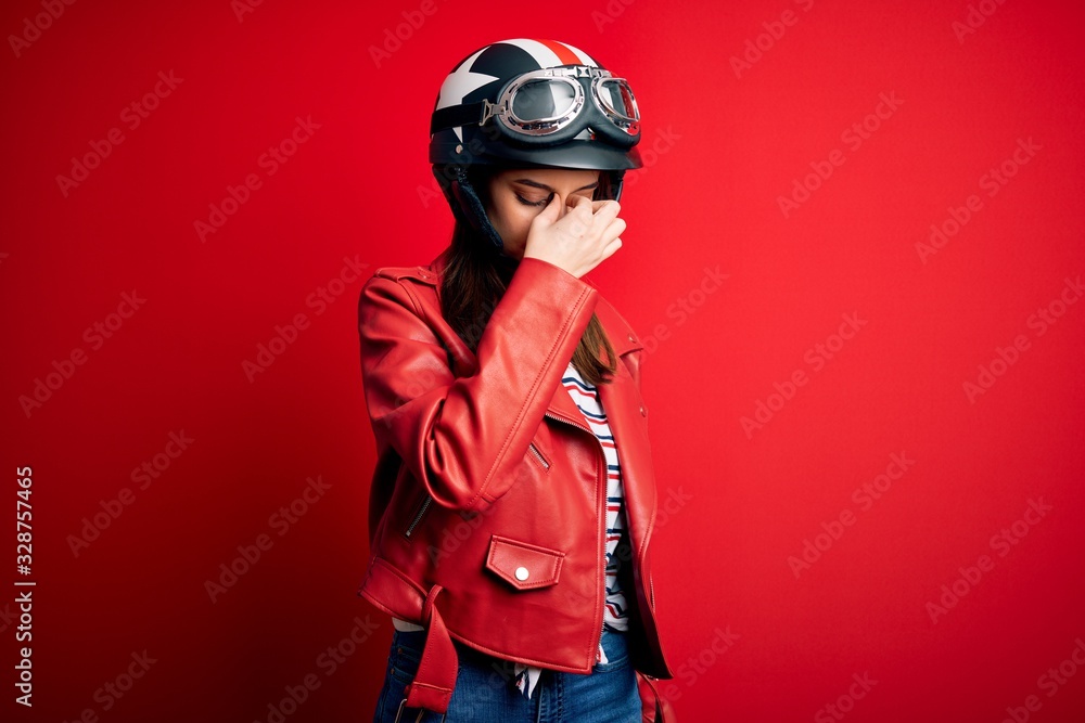Young beautiful brunette motocyclist woman wearing motorcycle helmet and red jacket tired rubbing nose and eyes feeling fatigue and headache. Stress and frustration concept. Young beautiful brunette motocyclist woman wearing motorcycle helmet and red jacket tired rubbing nose and eyes feeling fatigue and headache. Stress and frustration concept.