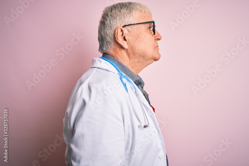 Senior handsome hoary doctor man wearing stethoscope and red HIV ribbon on coat looking to side, relax profile pose with natural face with confident smile. © Krakenimages.com