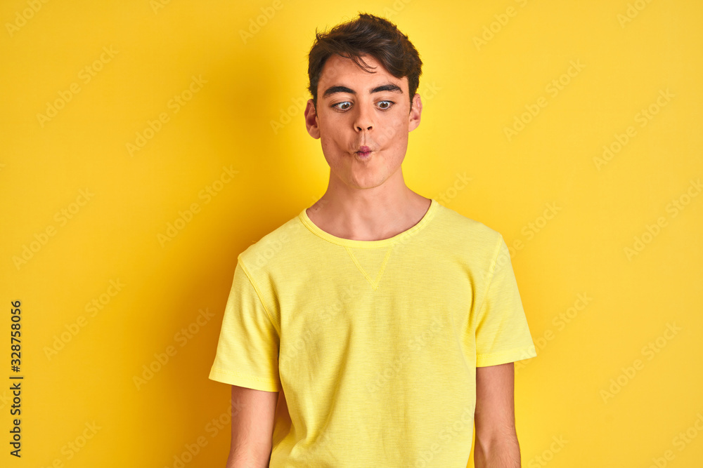 Fototapeta premium Teenager boy wearing yellow t-shirt over isolated background making fish face with lips, crazy and comical gesture. Funny expression.