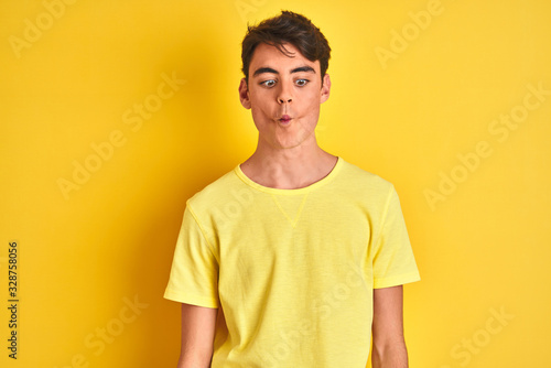 Teenager boy wearing yellow t-shirt over isolated background making fish face with lips, crazy and comical gesture. Funny expression. © Krakenimages.com