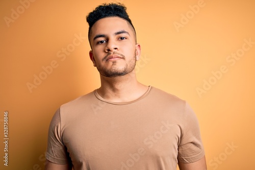 Young handsome man wearing casual t-shirt standing over isolated yellow background Relaxed with serious expression on face. Simple and natural looking at the camera.