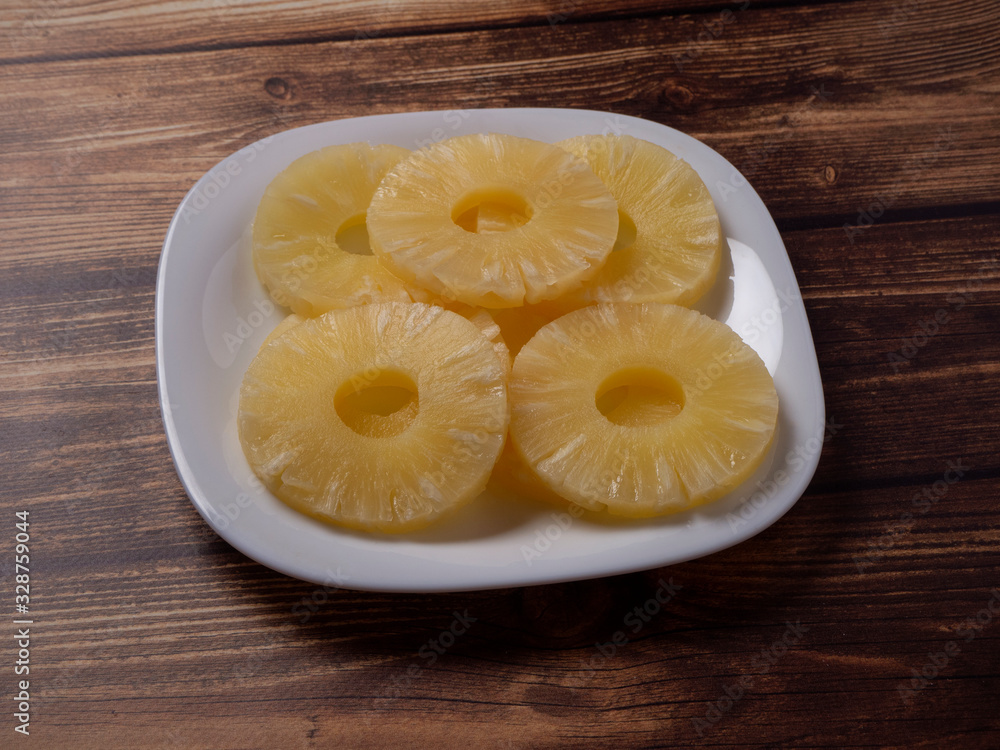 Yellow pineapple rings on a white plate on a wooden table close up. Chopped caramelized canned pineapple. Yellow pineapple rings on a white plate on a wooden table close up. Chopped caramelized canned pineapple.